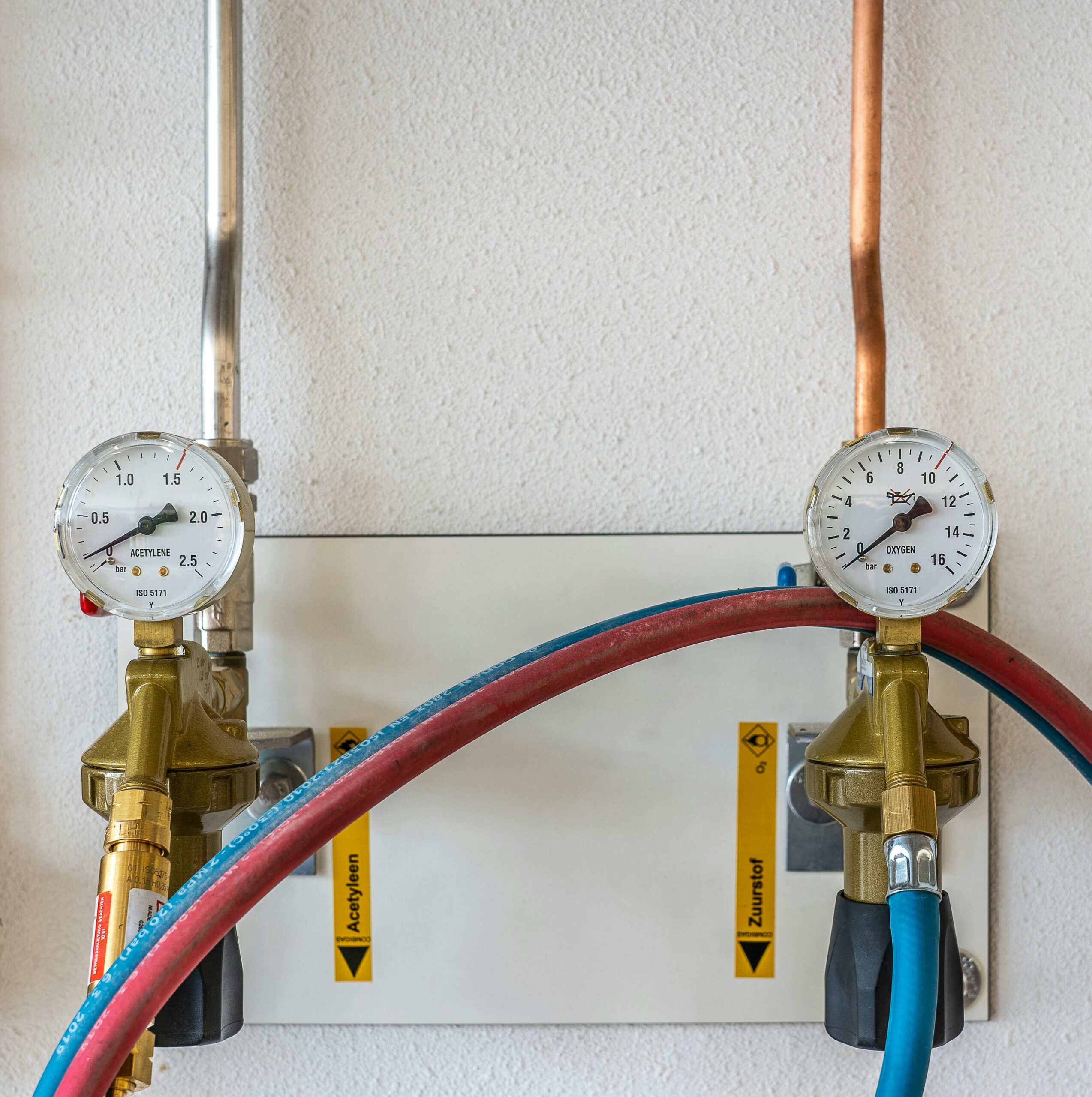 خدمات المعايرة والتحقق Close-up of industrial gas pressure gauges connected with hoses against a white wall.